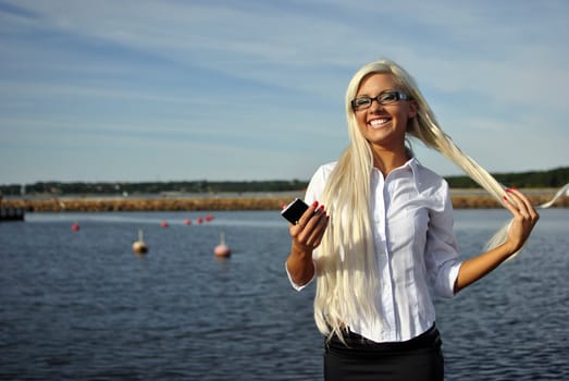 Blonde girl standing with mobile phone on the beach