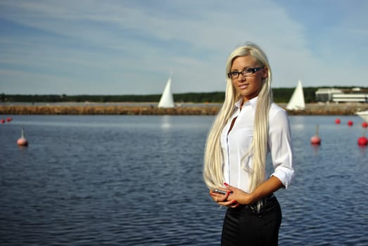 Blonde girl standing with mobile phone on the beach