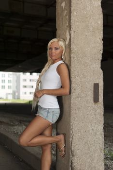 athletic girl in denim shorts and white T-shirt standing at the pillar