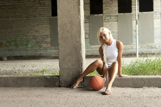 Beautiful blonde girl is sitting with basketball on the street