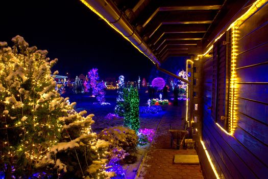 Christmas fantasy - trees and wooden house in lights on a beautiful winter evening