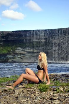 girl in bikini sitting near a waterfall