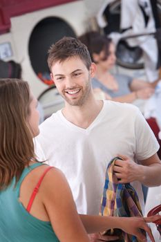 Young handsome Caucasian man flirts with woman in laundromat
