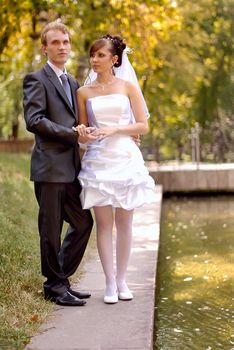 The bride and groom, standing near the lake in the park on a beautiful sunny day