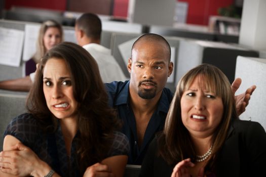 Handsome African-American man stands behind uncomfortable woman employees