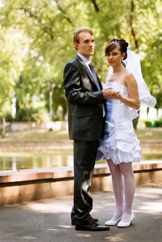 A young couple, the bride and groom, standing in the park, holding hands