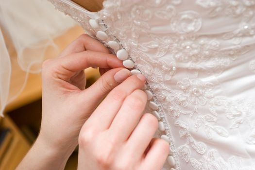 hands of a person help to a bride to clasp buttones of the dress