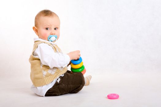 The toddler boy seats on floor and plays developing game. Color pyramidion.