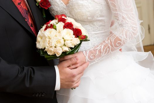 bouquet of red and white roses in the hands of newly married couple