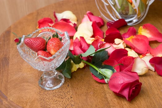 strawberry in a vase, red rose on the table and petals of red roses