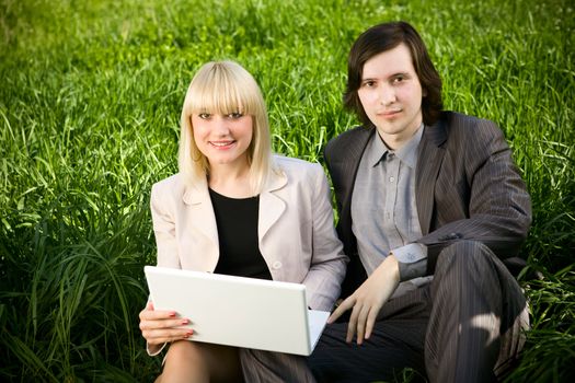 a young business man and business woman working on laptop in nature on the grass field