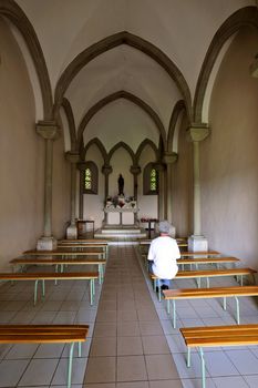 Inside a small chapel with a single worshipper sitting on a bench.