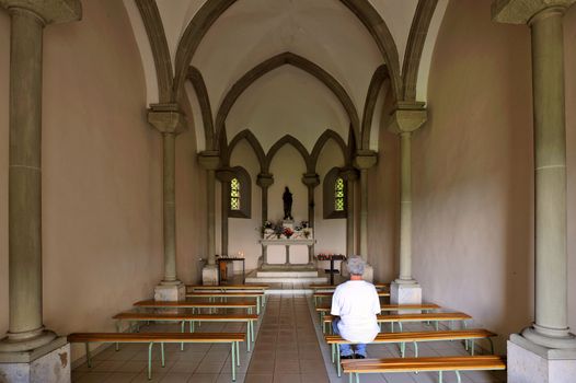 Inside a small chapel with a single worshipper sitting on a bench.