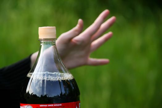 Human hand and bottle of Coca-Cola on green backgroud