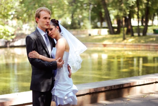 Young bride and groom embracing, standing in a park on a beautiful sunny day