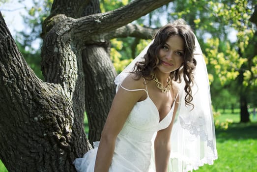 Attractive Bride stands about trees in the park