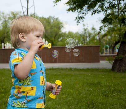 The boy blows soap bubbles in park