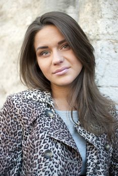 girl in leopard coat standing on the street, near the wall. portrait.
