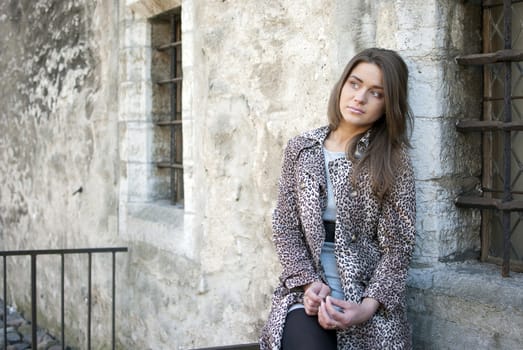 girl in leopard coat siiting on the street, near the window of old bulidingl
