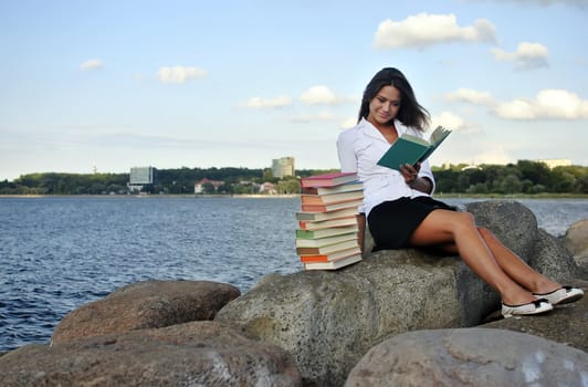 girl with books sitting on a rock by the sea