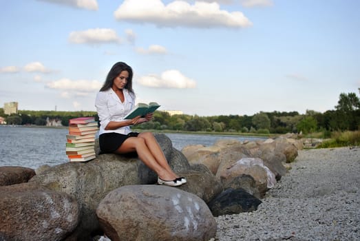 girl with books sitting on a rock by the sea