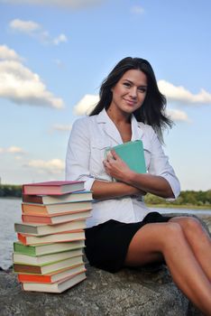 girl with books sitting on a rock by the sea