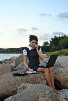office by the sea: the girl on the rocks with a laptop and a desktop phone signing papers