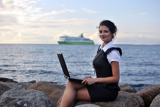 office by the sea: the girl on the rocks with a laptop. ship on the backdrop.