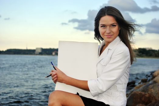 beautiful girl in a white jacket holding blank paper. sea on the background