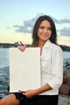 beautiful girl in a white jacket holding blank paper. sea on the background