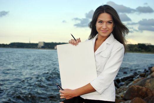 beautiful girl in a white jacket holding blank paper. sea on the background