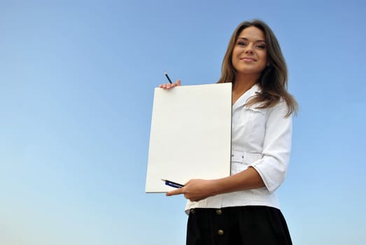 beautiful girl in a white jacket holding blank paper. sea on the background