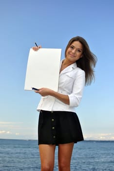 beautiful girl in a white jacket holding blank paper. sea on the background