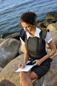beautiful girl with a notebook and a calculator sitting on the rocks