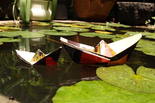 Boats made of paper in a pond with waterlily leaves.