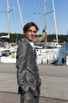 man in a gray suit, standing on the beach near the yacht
