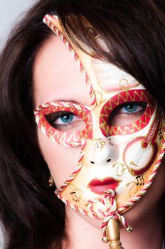 Beautiful young brunette haired, blue eyed sexy model dressed in gold with colourful red and gold venetian carnival face mask