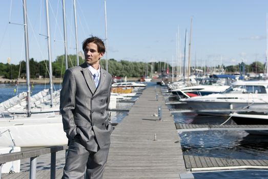 man in a gray suit, standing on the beach near the yacht