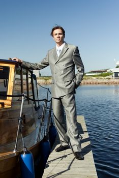 man in a gray suit, standing on the beach near the yacht