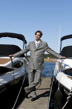 man in a gray suit, standing on the beach near the yacht