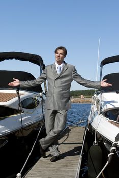 man in a gray suit, standing on the beach near the yacht