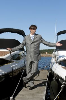 man in a gray suit, standing on the beach near the yacht