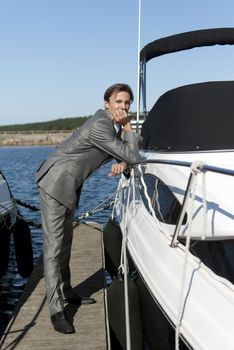 man in a gray suit, standing on the beach near the yacht