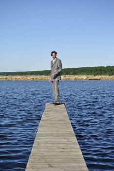 man in a gray business suit standing on a pier near the sea