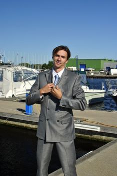man in a gray business suit straightens his tie, in the background of yachts