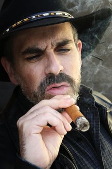 Man with beard in cowboy hat smoking cigar