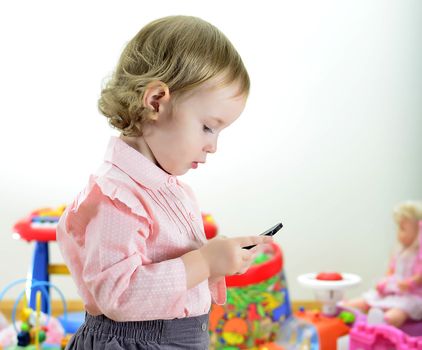 little girl standing with mobile phone in room with toys