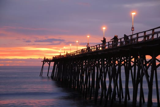 The sunrise over the pier at Kure Beach with fisherman on the pier.
