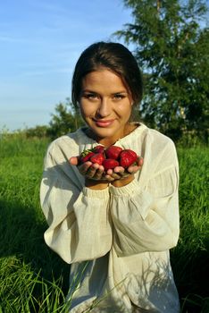 girl in a linen shirt, holding a strawberry in hand. focus on berries