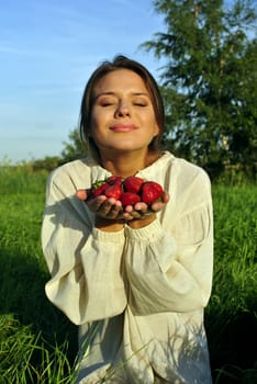 girl in a linen shirt, holding a strawberry in hand. focus on berries